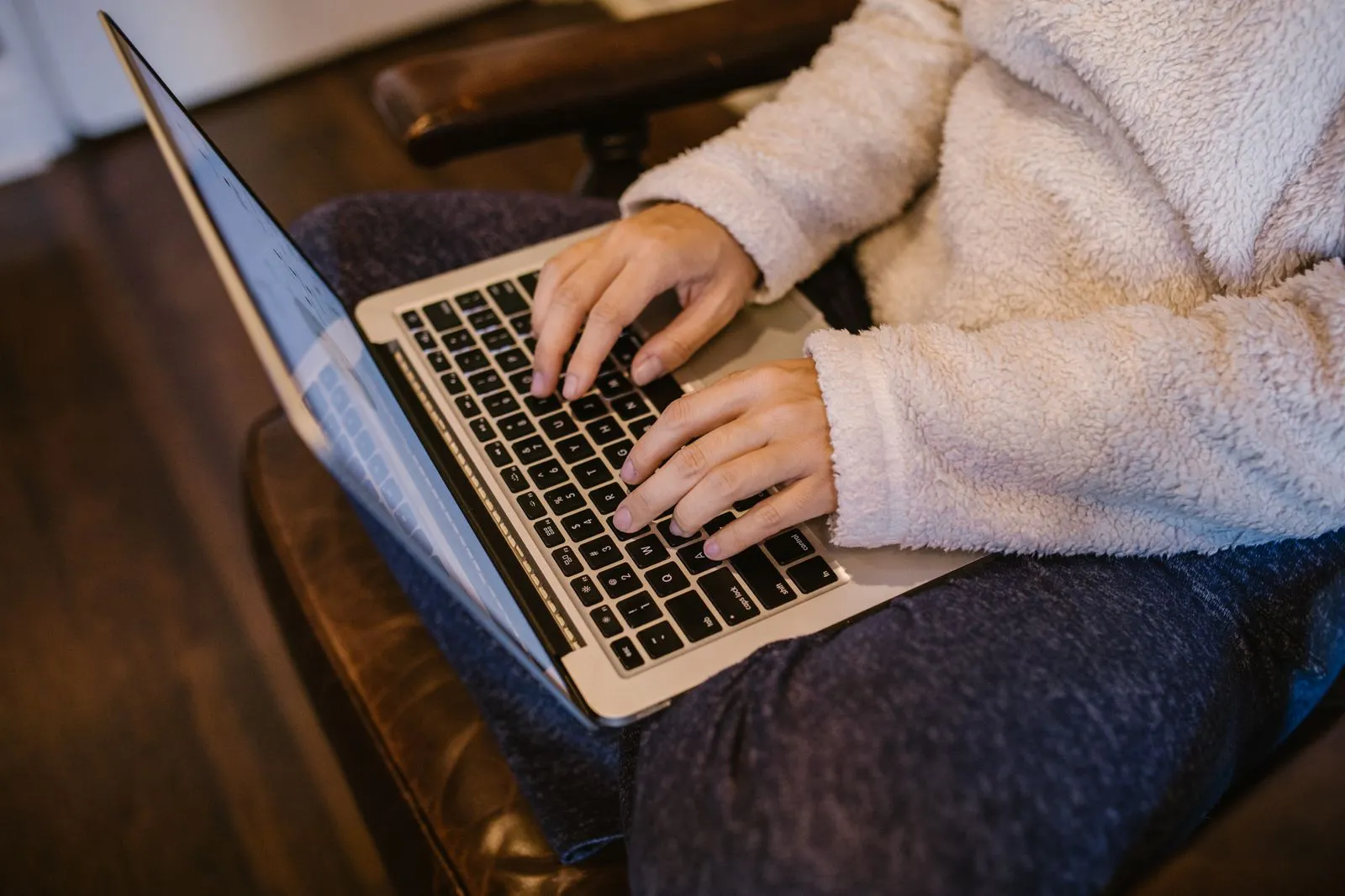 Hands typing on a laptop, a fleece sweater sleeve in a warm room
