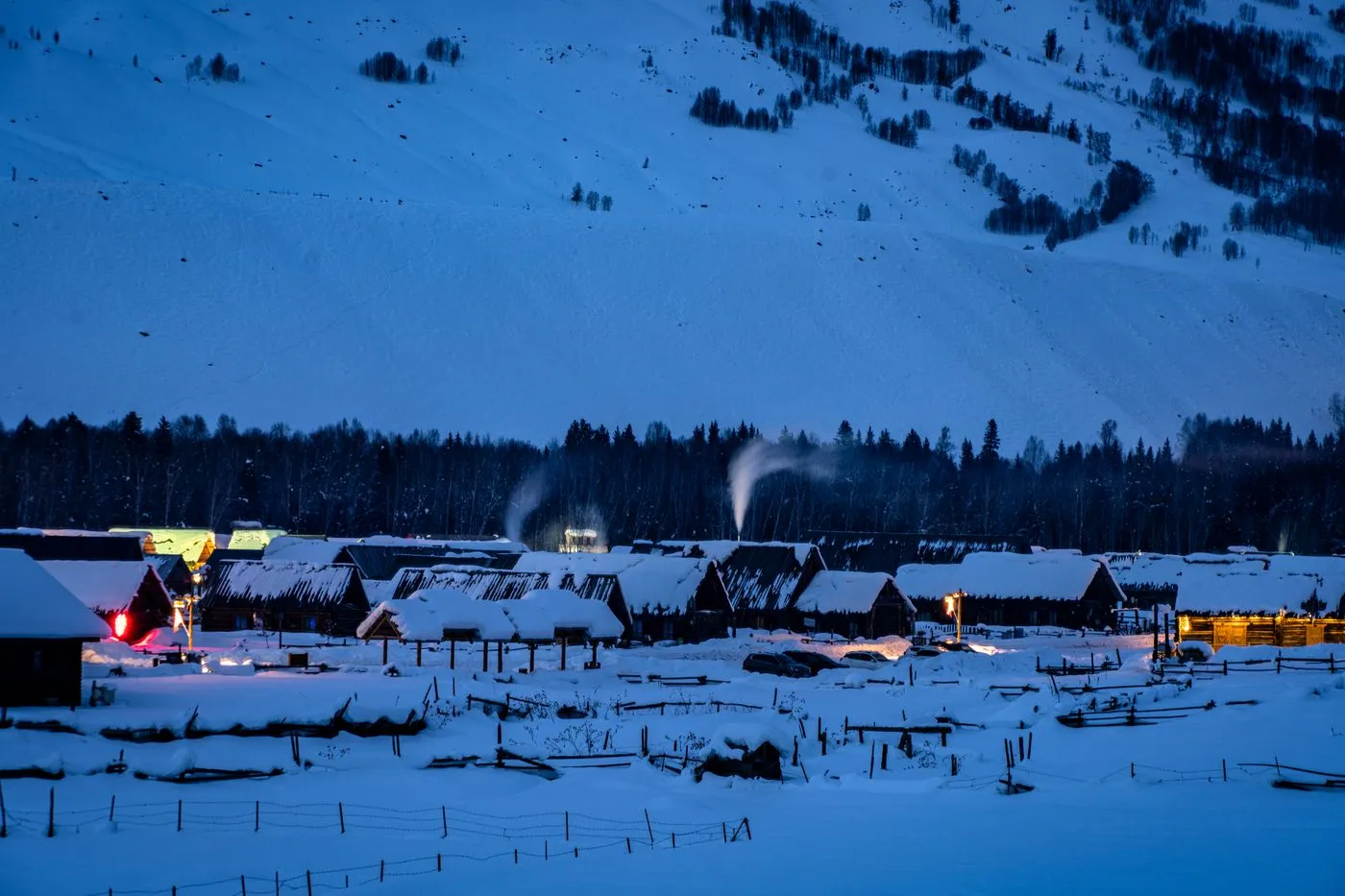 A snowy log-cabin village at blue hour with warm lit windows