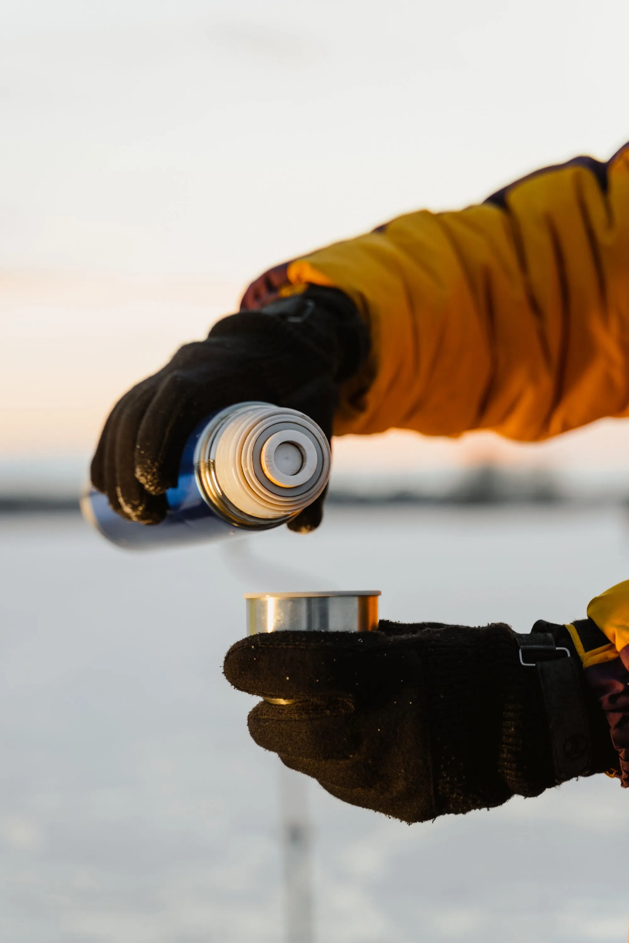 Gloved hands pouring a hot drink, standing in for the Ember Puck Mini Hand Warmer