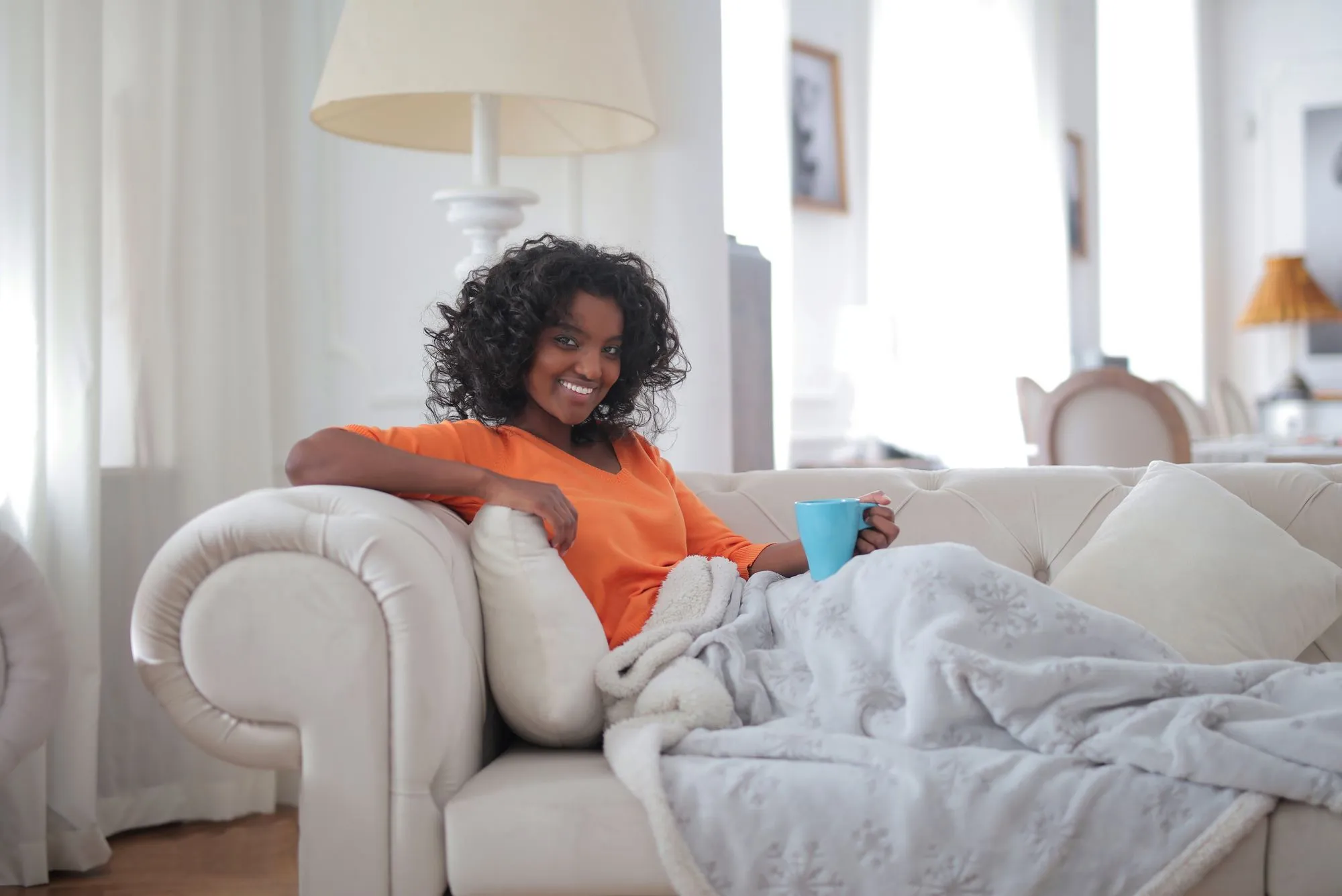 A woman resting under a soft blanket on a sofa, standing in for the Marlow Sherpa Heated Blanket