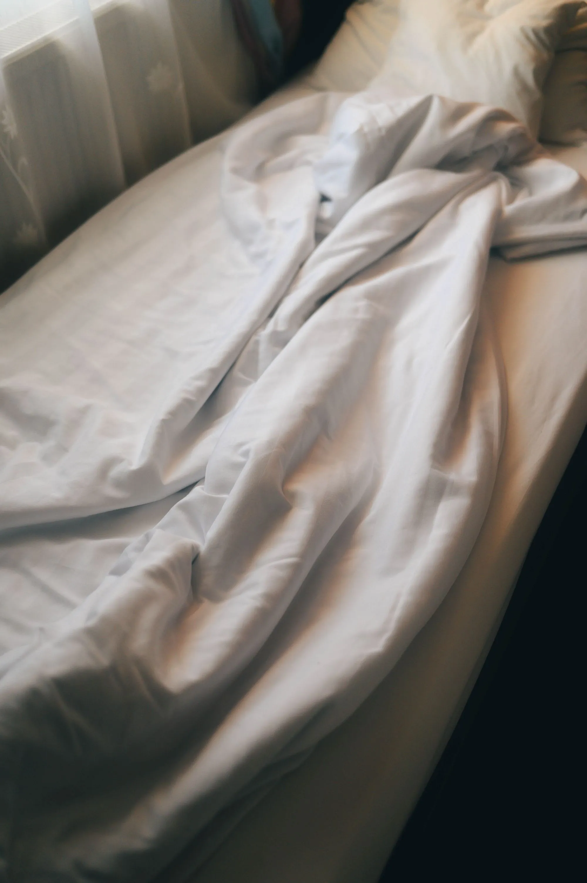 Crinkled white sheets on a mattress in warm morning light