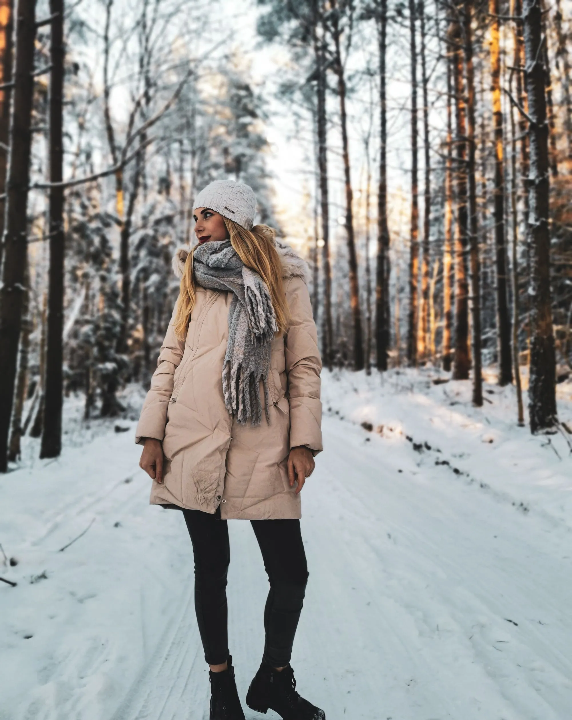 A woman in a long winter coat and a knit scarf in a snowy forest